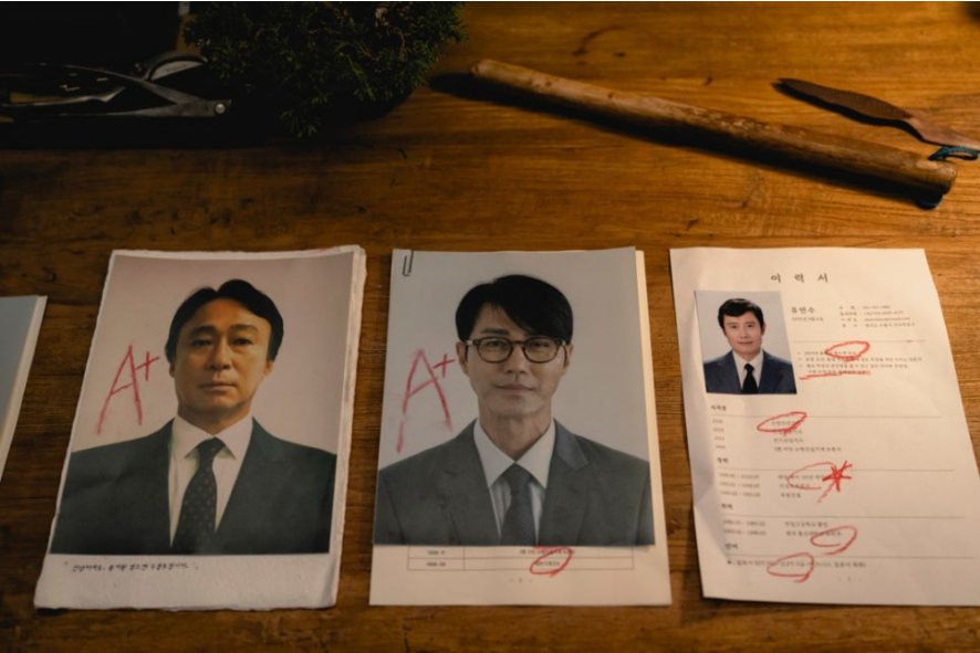 책상 위에 놓인 두 명의 지원자 사진에는 A+라는 등급이, 오른쪽에 있는 이력서(유만수)에는 붉은색으로 밑줄과 X 표시가 처참하게 그어져 있습니다.